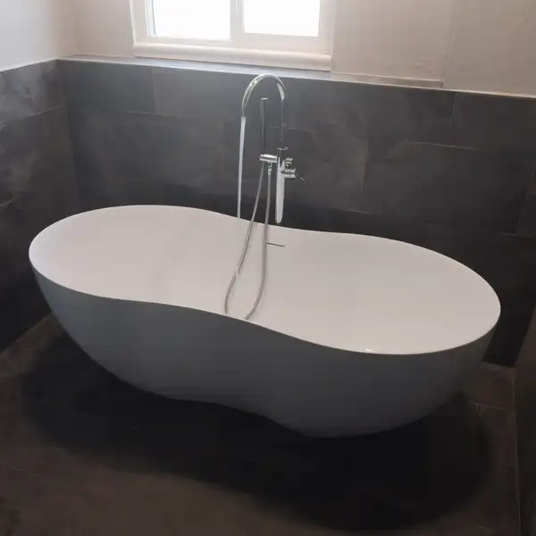 Freestanding soaking tub with a floor-mounted filler on dark tile