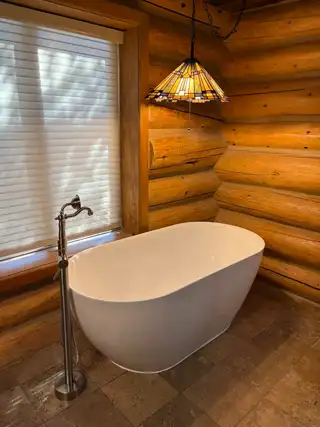 Freestanding tub with a floor-mounted filler in a log-cabin bathroom