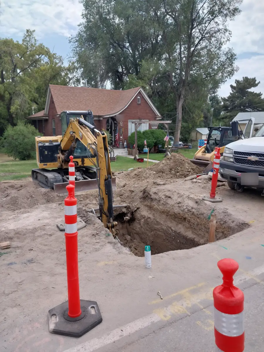 Mini excavator digging a sewer line trench in front of a brick home
