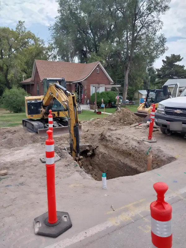 Mini excavator digging a sewer line trench in front of a brick home