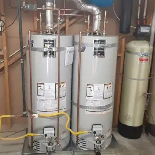 Two gas water heaters installed side by side next to a water softener